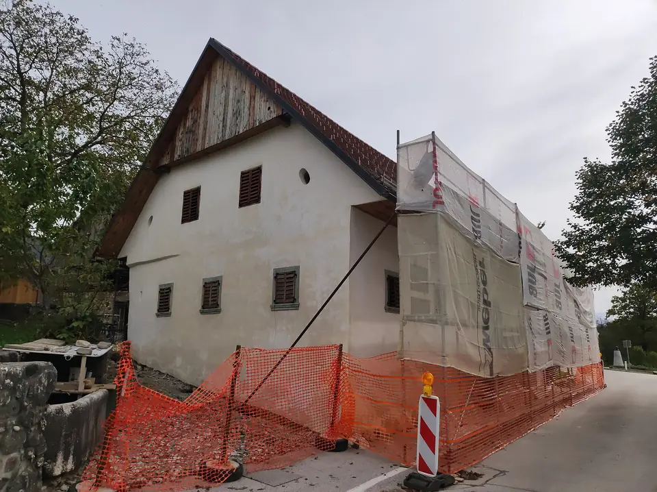 Maison ancienne en cours de rénovation à Vrba, façade enveloppée d'un échafaudage bâché et chantier délimité par une clôture orange.